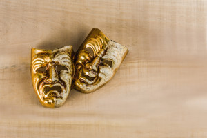 Two theatrical masks of joy and sadness lie on a wooden table